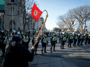 A man carrying a Mohawk Warrior Flag faces a line of Parliamentary Protective Service officers during the All Eyes on Parliament: Rally for the Wet'suwet'en in downtown Ottawa. February 24, 2020.