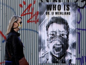 A woman in Prague, Czech Republic, passes a poster of Dr. Li Wenliang, the Chinese ophthalmologist who was silenced by the authorities when he tried to warn the Chinese medical community about COVID-19, and who subsequently died of the illness at a hospital in Wuhan.