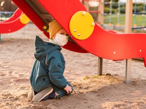 A child in a medical mask plays on the playground during the pandemic of coronavirus and Covid - 19