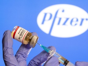 A woman holds a small bottle labeled with a "Coronavirus COVID-19 Vaccine" sticker and a medical syringe in front of displayed Pfizer logo in this illustration taken, October 30, 2020.