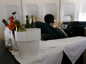 With bottles of wine in the foreground, a passenger watches a movie inside the first class cabin of a commercial passenger 747-400 airplane.
