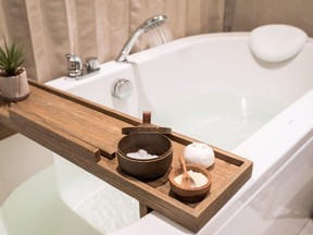 Modern and comfortable bathroom, Bath tub with wooden table and toiletries, Salt, Herb, Bath Bomb.