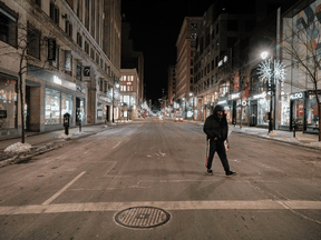 A man carrying a blanket and other possessions crosses Saint Catherine St. in Montreal on January 9, 2021, about an hour after the 8 p.m. curfew went into effect.