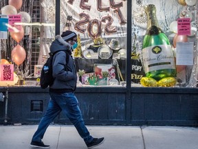 A pedestrian wearing a mask walks past a store selling party items with signage stating “Hello 2021” on Toronto's Danforth Avenue during the Covid 19 pandemic, Monday January 11, 2021.