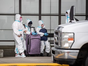People wearing protective face masks, goggles and Tyvek suits who said they traveled from Colombia wait for a car rental company shuttle, after arriving at Vancouver International Airport in Richmond, B.C., on Thursday, December 31, 2020.