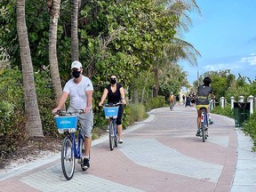 Tourists wear masks as they bike along the beach in Miami, Florida, on December 20, 2020, amid the Coronavirus pandemic. Birds of a feather flock together, but the pandemic has firmly wedged Canada's infamous "snowbirds" in two camps: those staying home and those heading to Florida this winter no matter the cost, financial or otherwise.