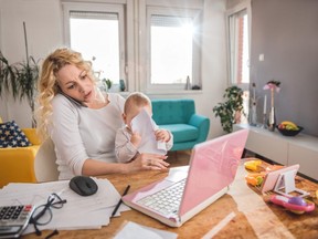 Worried mother holding baby and talking on smart phone at home office