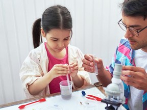 Father and his daughter doing science experiments in the laboratory. Dad and little girl study chemistry lesson with microscope, mixing liquids in the flasks for lab experiment. Homeschooling concept.