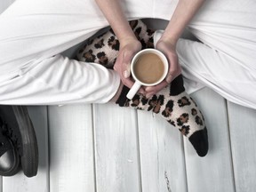 Teenage girl sitting on floor holding a cup of coffee. Body part close up on wooden surface