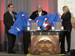 Justice Murray Sinclair, centre, Chief Wilton Littlechild, left, and Marie Wilson pull back a blanket to unveil the Final Report of the Truth and Reconciliation Commission of Canada on the history of Canada's residential school system, in Ottawa in 2015.