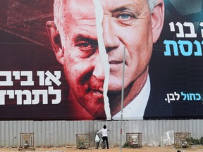 A boy looks up at a Blue and White party election campaign banner depicting its leader, Israeli defence minister Benny Gantz, alongside Israeli Prime Minister Benjamin Netanyahu, ahead of the March 23 ballot, in Bnei Brak, Israel.