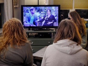 This photo illustration shows people wearing face masks, watch a televised conversation between Britain's Prince Harry with his wife Meghan Markle and US host Oprah Winfrey, in Arlington, Virginia March 7, 2021.