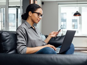 Young woman making online payment while sitting in the living room on sofa