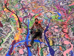 Contemporary British artist Sacha Jafri (C) sits on his record-breaking painting entitled 'The Journey of Humanity' on September 23, 2020, as he speaks to people in the Emirati city of Dubai.