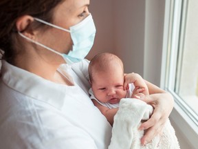 A woman wearing a mask holds a newborn baby. Scientists have found evidence of the COVID-19 virus mutating in a newborn baby five days after it was born.