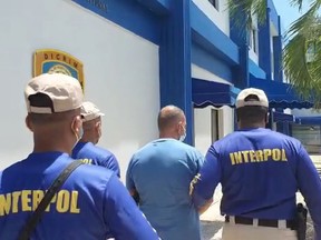 Interpol officers escort Marc Feren Claude Biart, 53, a mafia fugitive who was tracked down thanks to his tattoos visible in cooking videos he posted on YouTube, after arresting him in Boca Chica, Dominican Republic, in this still image taken from video filmed on March 24, 2021.