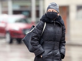 A woman wearing a mask crosses Portage Avenue in Winnipeg on March 21, 2021.