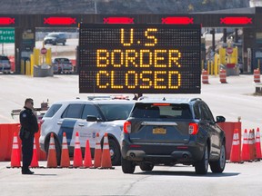 US Customs officers speak with occupants of a vehicle at the US/Canada border in Lansdowne, Ont., on March 2020.