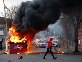 A man walks past a hijacked bus burning on The Shankill Road as protests continue in Belfast, Northern Ireland, April 7