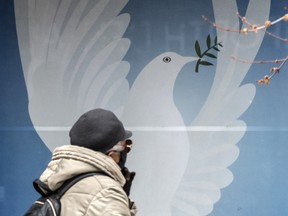 A pedestrian wearing a mask walks past a image of a dove on Toronto’s Danforth Avenue on April 1.