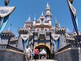 Guests wearing protective masks cross the bridge in front of Sleeping Beauty Castle during the reopening of the Disneyland theme park in Anaheim, California, on Friday, April 30, 2021.