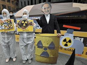 South Korean activists wearing protective clothing and a mask of Japan's Prime Minister Yoshihide Suga perform during a protest against Japan's decision on releasing Fukushima wastewater, near the Japanese embassy in Seoul on April 13, 2021.