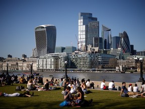 Pedestrians relax in the sunshine in a park on the south bank of the River Thames in view of skyscrapers in the City of London, on Monday, March 29, 2021.