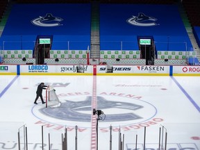 An arena worker removes the net from the ice after the Vancouver Canucks and Calgary Flames NHL hockey game was postponed due to a positive COVID-19 test result, in Vancouver, on Wednesday, March 31, 2021.