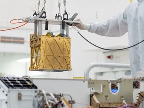 Technicians at NASA's Jet Propulsion Laboratory lower the Mars Oxygen In-Situ Resource Utilization Experiment (MOXIE) instrument into the belly of the Perseverance rover in an undated photograph in Pasadena, California