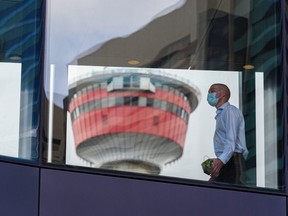 A masked pedestrian walks on the plus-15 in downtown Calgary with the Calgary Tower in the background on Tuesday, May 4, 2021.