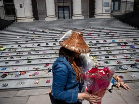 A woman carries flowers to be placed with 215 pairs of children's shoes on the steps of the Vancouver Art Gallery as a memorial to the 215 children whose remains have been found buried at the site of a former residential school in Kamloops.