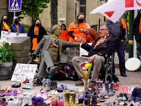 Elder Junior Peter Paul (sitting) points to a Sir John A. MacDonald statue next to 215 pairs of children's shoes placed in remembrance of the bodies discovered at the Kamloops Indian Residential School in British Columbia during a ceremony in Charlottetown, on Monday, May 31.