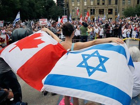 A participant waves Canadian and Israeli flags at a pro-Israel rally at Calgary city hall in a file photo from July 31, 2014. Canada has announced it is boycotting the Durban IV conference in New York this September due to anti-Semitism and the anti-Israel nature of the original event in 2001.