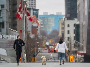 A jogger keeps his distance from a woman walking her dog in downtown Toronto, Ontario on March 24, 2020.