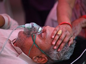 A relative comforts a Covid-19 coronavirus patient breathing with the help of oxygen provided by a Gurdwara, a place of worship for Sikhs, under a tent installed along the roadside amid Covid-19 coronavirus pandemic in Ghaziabad on May 2, 2021.