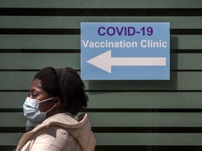 A pedestrian wearing a mask walks past signage for a vaccination clinic on Toronto's CAMH buildings on April 28, 2021.