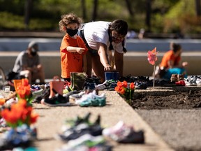 A mother and child leave a pair of children's rubber boots in memory of 215 children whose remains were found in unmarked graves at the site of the Kamloops Indian Residential School during a vigil at the "Service through Christ" statue at the Alberta Legislature in Edmonton on May 30, 2021.