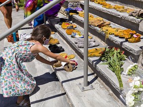A youngster places a pair of moccasins on the steps of the former Mohawk Institute Residential School in Brantford, Ont., on May 30, 2021, in honour of the 215 children whose remains were found in unmarked graves at a former residential school in Kamloops, B.C. A survivor of the Brantford school suggests renaming Ryerson University in honour of War of 1812 hero Chief Tecumseh.