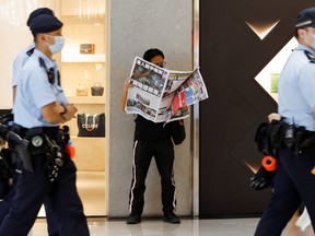 Police patrol past an Apple Daily supporter as he reads the final edition of the newspaper at a shopping mall in Hong Kong, China on June 24, 2021.