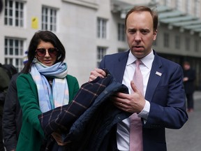 Britain's Health Secretary Matt Hancock hands his coat to his aide, Gina Coladangelo, before a television interview in London in a file photo from May 16, 2021. Hancock has resigned after the leak of a photo of him embracing Coladangelo.