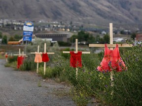 Children's dresses are staked along a highway near the former Kamloops Indian Residential School, where flowers and cards have been left as part of a growing memorial to honour the 215 children whose remains have been discovered buried in undocumented graves on the property, in Kamloops, B.C., on June 2, 2021.