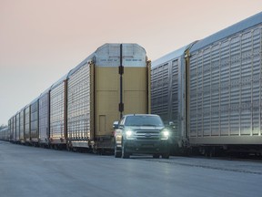 A prototype of the all-electric Ford F-150 Lightning pulls 10 rail cars loaded with 42 Ford trucks