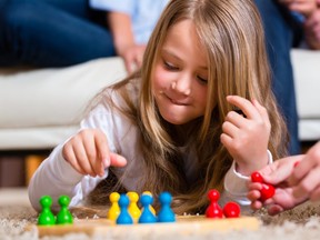 Family playing board game ludo at home on the floor, close up on child