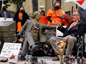 Elder Junior Peter Paul (sitting) points to a Sir John A. MacDonald statue in Charlottetown, next to 215 pairs of children's shoes placed in remembrance of the children's graves discovered at the Kamloops Indian Residential School, May 31, 2021. The statue has since been removed.