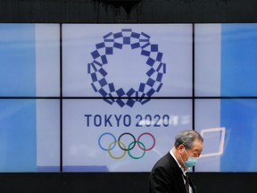 A passerby wearing a protective face mask walks past a screen showing the logo of the 2020 Olympic Games in Tokyo, Japan, on April 14, 2021.