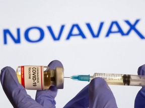 A woman holds a small bottle labeled with a "Coronavirus COVID-19 Vaccine" sticker and a medical syringe in front of displayed Novavax logo in this photo taken on October 30, 2020.