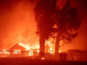 A firefighter works the scene as wind-whipped flames and embers light homes on fire in San Bernardino.