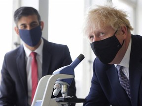 In this file photo, Britain's Chancellor of the Exchequer Rishi Sunak (left) watches as Britain's Prime Minister Boris Johnson (right), looks through a microscope as he takes part in a science lesson at King Solomon Academy in London, on April 29, 2021.