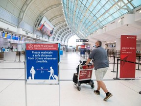 In this file photo, a man pushes a baggage cart while wearing a mandatory face mask at Toronto Pearson International Airport in Toronto, on June 23, 2020.