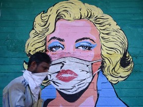 A pedestrian walks past a mural of Marilyn Monroe wearing a face mask.